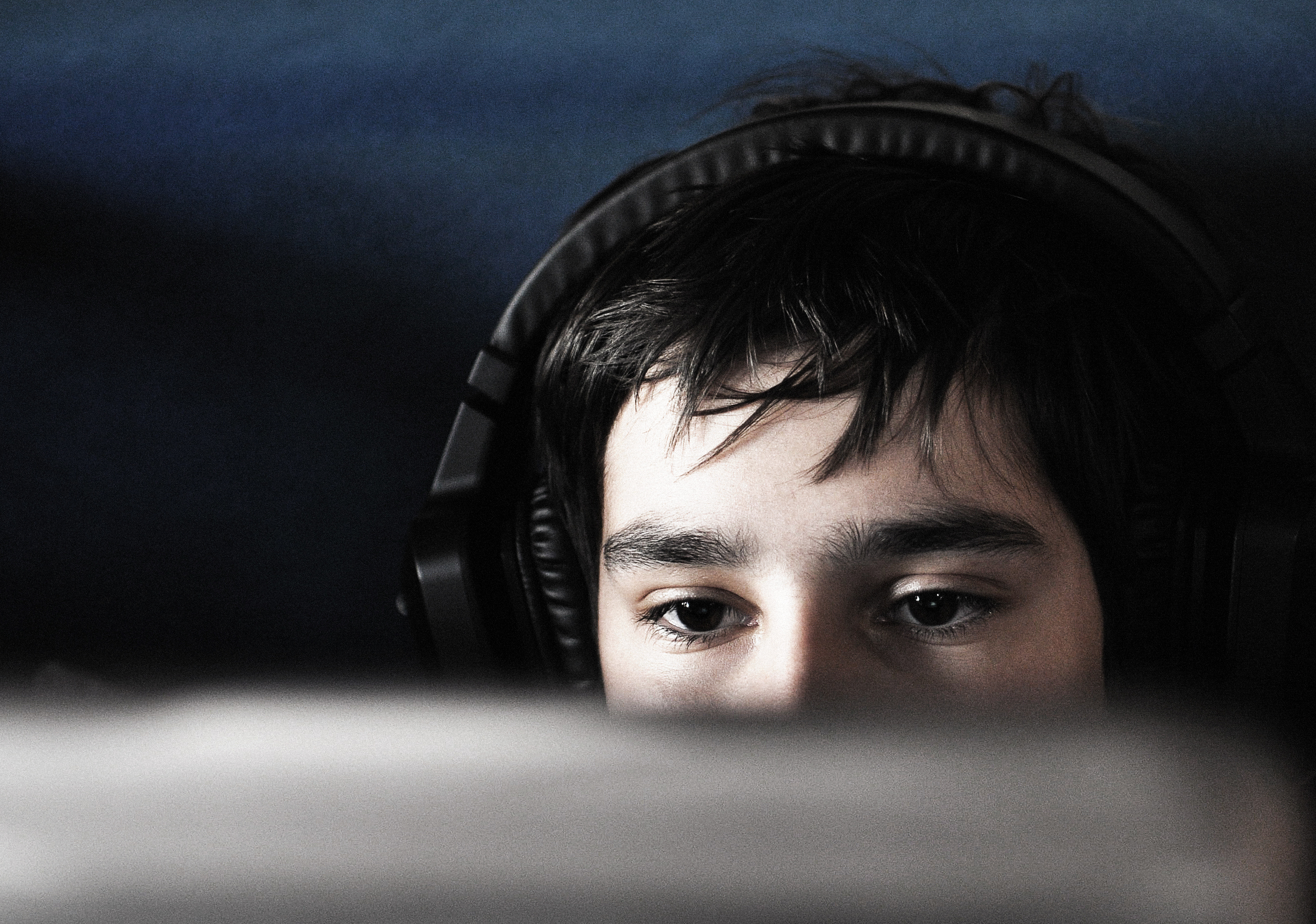 Young person with headphones staring at a computer screen late at night.