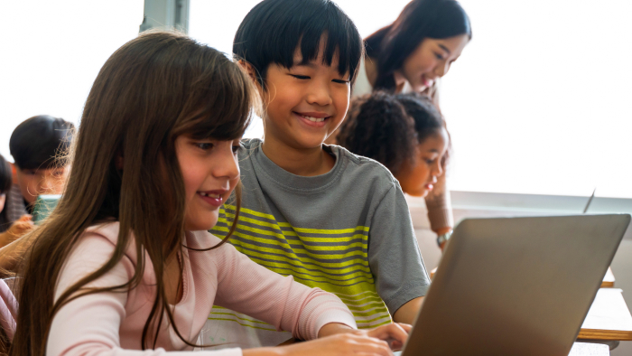 A girl with white skin and a boy of Asian descent smile while looking at a computer.