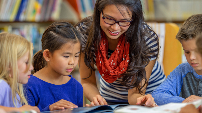 Asian-appearing teacher works with diverse group of students.