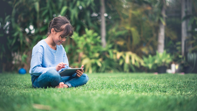 girl on the lawn reading on an ipad