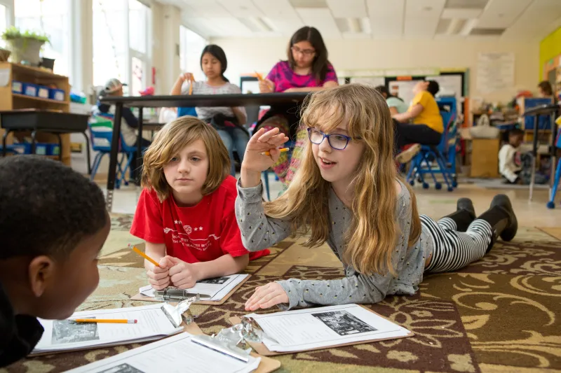 A photo of elementary students lying on a library floor doing a project together