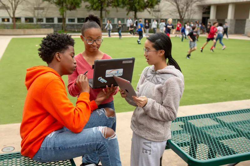 A photo of three middle schoolers sharing a computer to complete an assignment