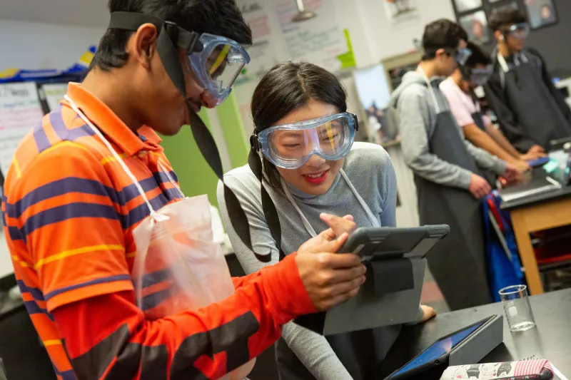 A photo of two students using a tablet as they complete a chemistry lab assignment