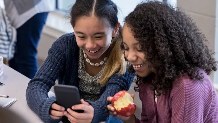 Photo of two students looking at a phone and smiling