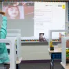 Students in a classroom wave to their online classmates